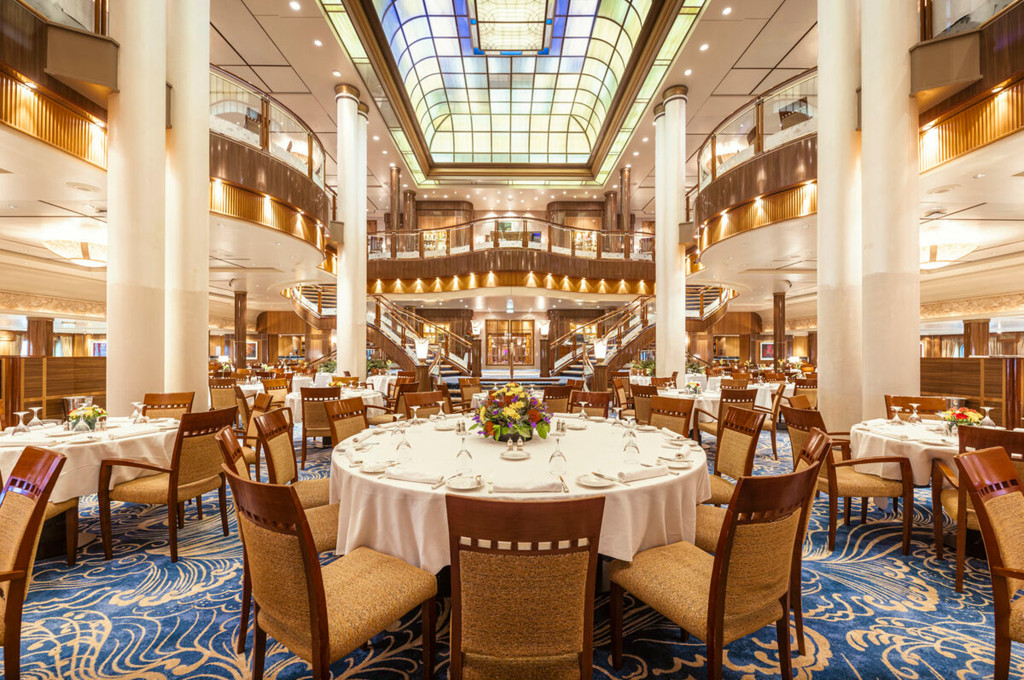 Großes Britannia Restaurant der Queen Mary 2 mit Glasdecke, geschwungener Doppeltreppe und weiß gedeckten Tischen