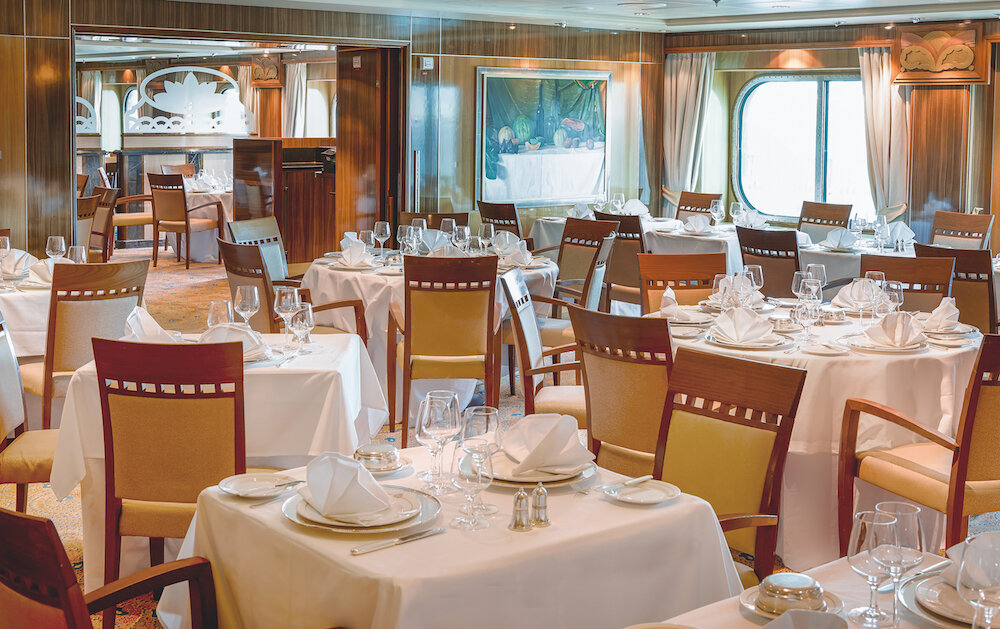 Britannia Restaurant mit elegant gedeckten Tischen und weißen Servietten auf einer Hochseekrreuzfahrt.