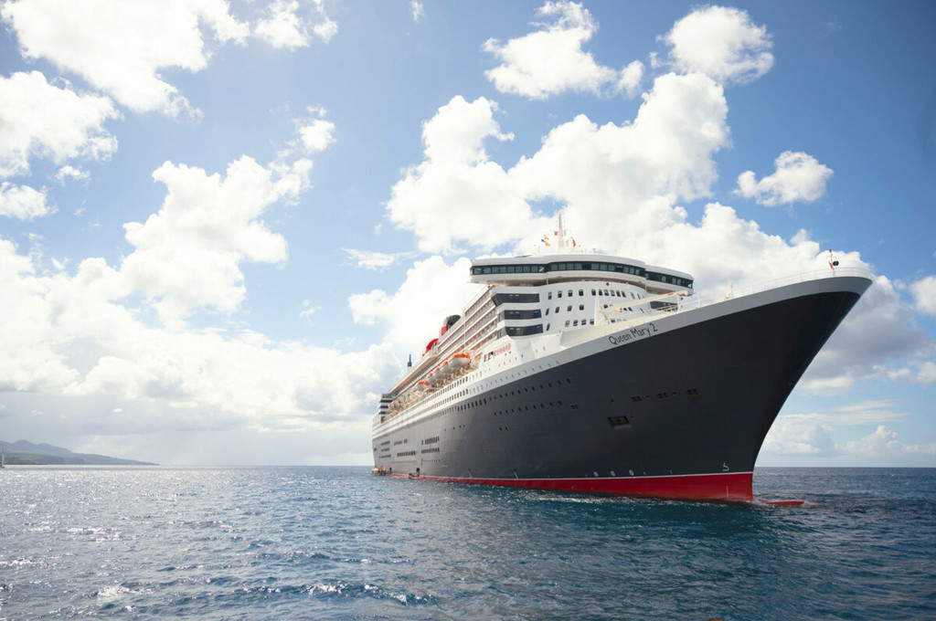 Klassische Seitenansicht der Queen Mary 2 auf See mit dunklem Rumpf, rotem Schornstein und blauem Himmel