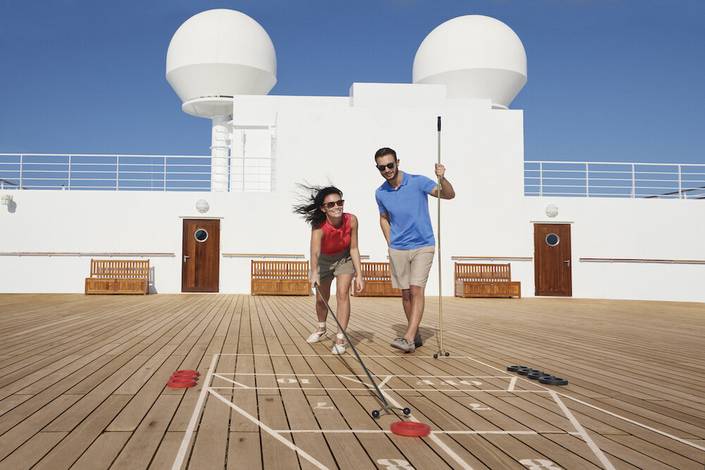 Paar spielt Shuffleboard auf dem Teakdeck der Queen Mary 2 bei sonnigem Wetter