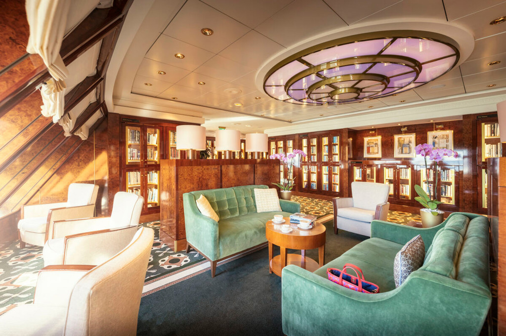 Elegante Bibliothek der Queen Mary 2 mit grünen Samtsofas, beleuchteten Bücherregalen und Orchideenschmuck