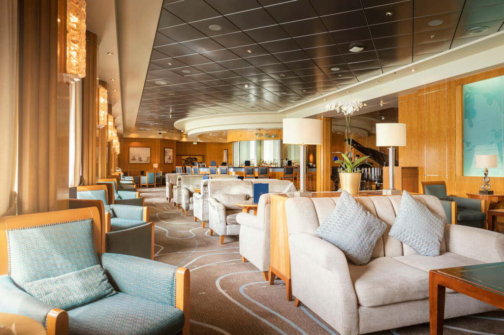 Weitläufige Carinthia Lounge der Queen Mary 2 mit Holzverkleidung, blauen Sesseln, weißen Sofas und Konzertflügel