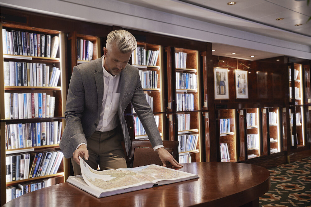 Elegante Bibliothek mit Holzbücherregalen und komfortablen Sesseln zum Lesen an Bord einer Hochseekreuzfahrt.
