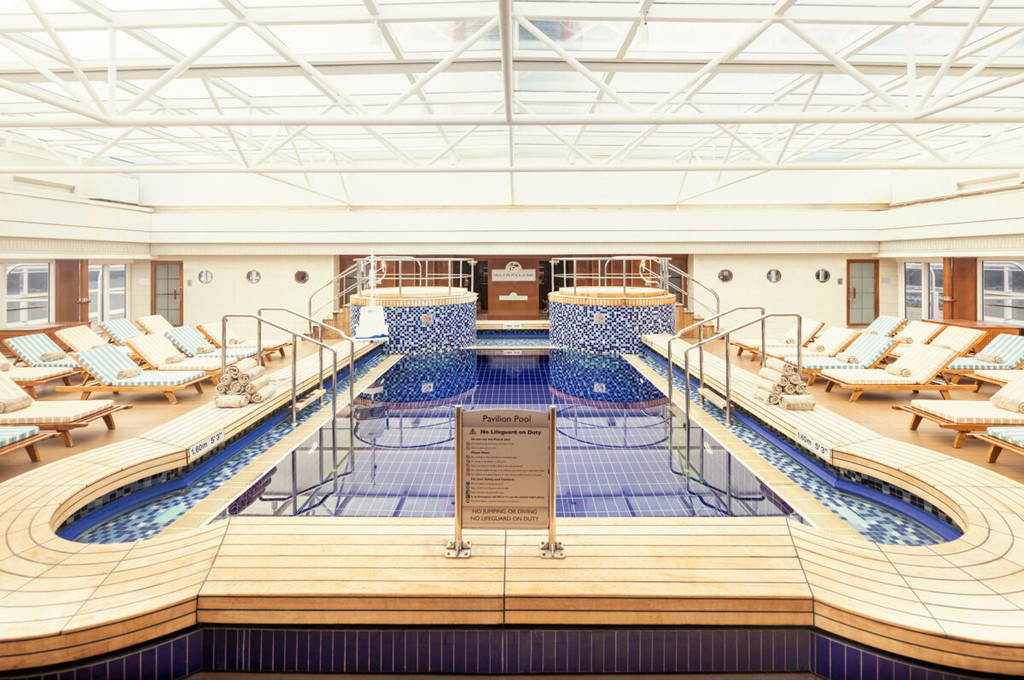 Überdachter Pavillon-Pool der Queen Mary 2 mit Glasdach, blauem Mosaikboden, zwei Whirlpools und gestreiften Liegestühlen