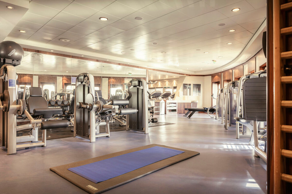 Fitnessraum der Queen Mary 2 mit Kraftgeräten, Spiegelwand und Yogamatte