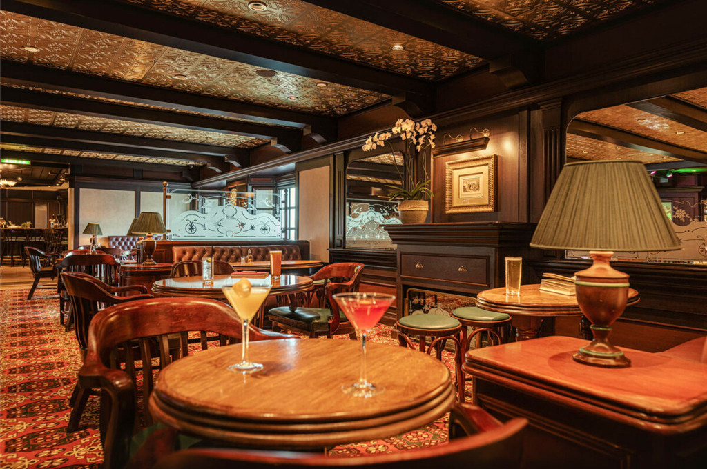 Golden Lion Pub der Queen Victoria mit dunklem Holzinterieur, Pressblechdecke und Cocktailgläsern auf runden Holztischen