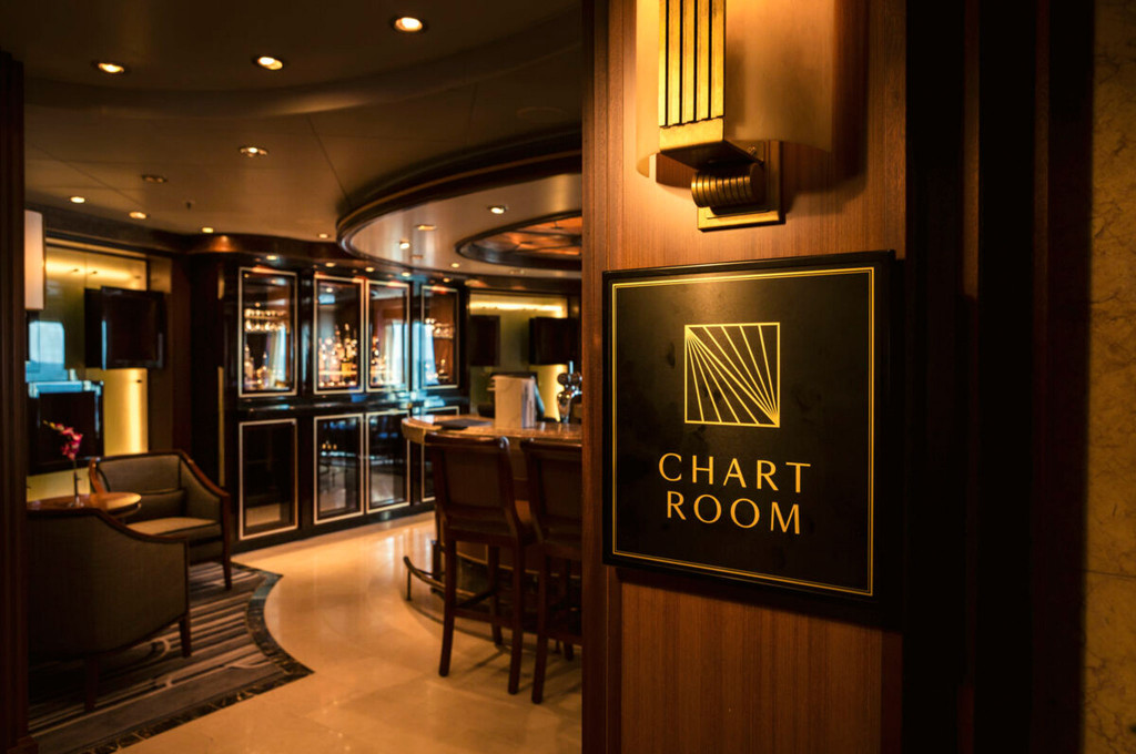 Eingang zum Chart Room der Queen Victoria mit goldenem Schriftzug auf dunklem Holzpaneel und beleuchteter Bar im Hintergrund