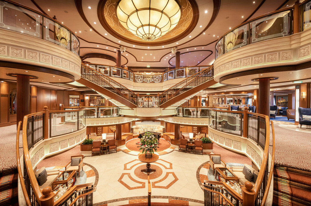 Prachtvoll ausgestattetes Grand Lobby der Queen Victoria mit geschwungener Doppeltreppe, drei Balkongalerien und großem Kronleuchter