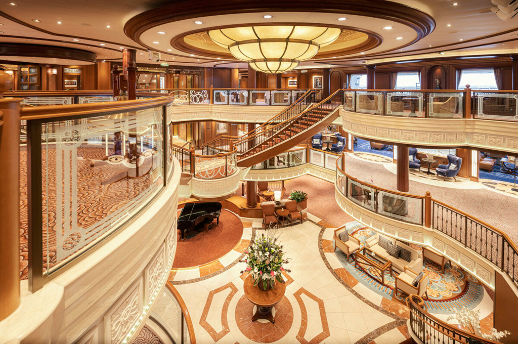 Blick von der Galerie auf das Grand Lobby der Queen Victoria mit Doppeltreppe, Flügel und Blumenarrangement