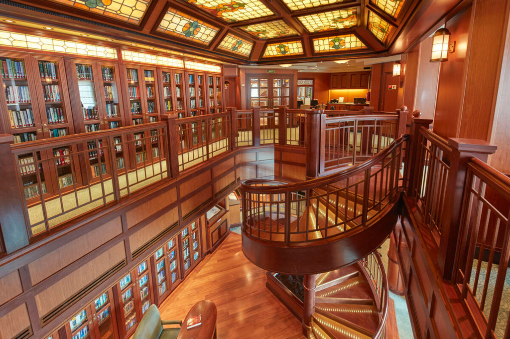 Zweigeschossige Bibliothek der Queen Victoria mit Tiffany-Glasdecke, mahagonifarbenen Bücherregalen und geschwungener Wendeltreppe