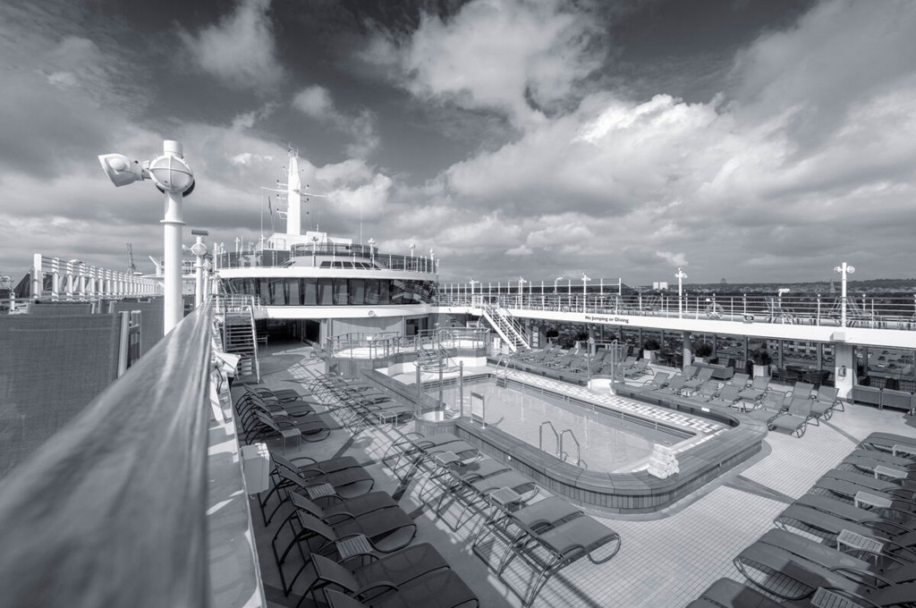 Sonnendeck der Queen Victoria mit großem Außenpool und Liegestühlen unter bewölktem Himmel