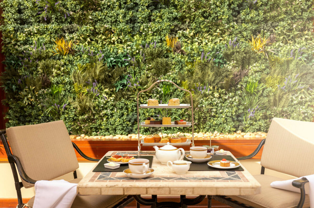 Grills-Terrasse der Queen Victoria mit Afternoon-Tea-Service, dreistöckigem Kuchenständer und grüner Pflanzenwand im Hintergrund