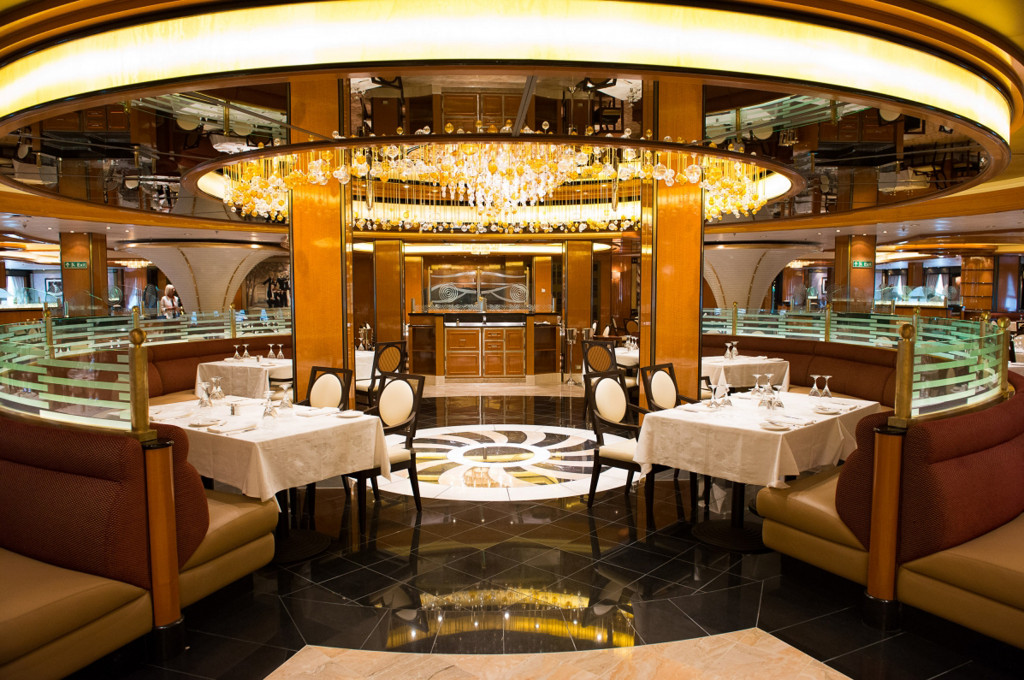 Das Haupt-Restaurant mit großem Kronleuchter, eleganten Sesseln und weißem Tischtuch auf der Royal Princess.