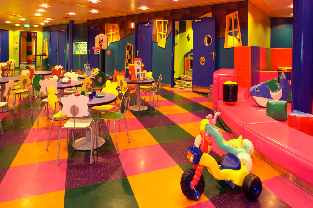 Kinderspielbereich Fun Zone mit buntem Karobodenbelag, Kindertischen, Basketballkorb und Spielgeräten.