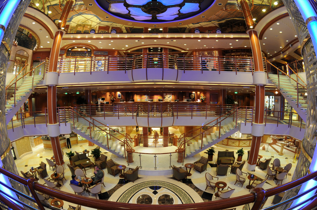 Mehrstöckiges Atrium mit geschwungenen Treppen, Rezeption und Sitzgruppen im Herzen des Schiffes.