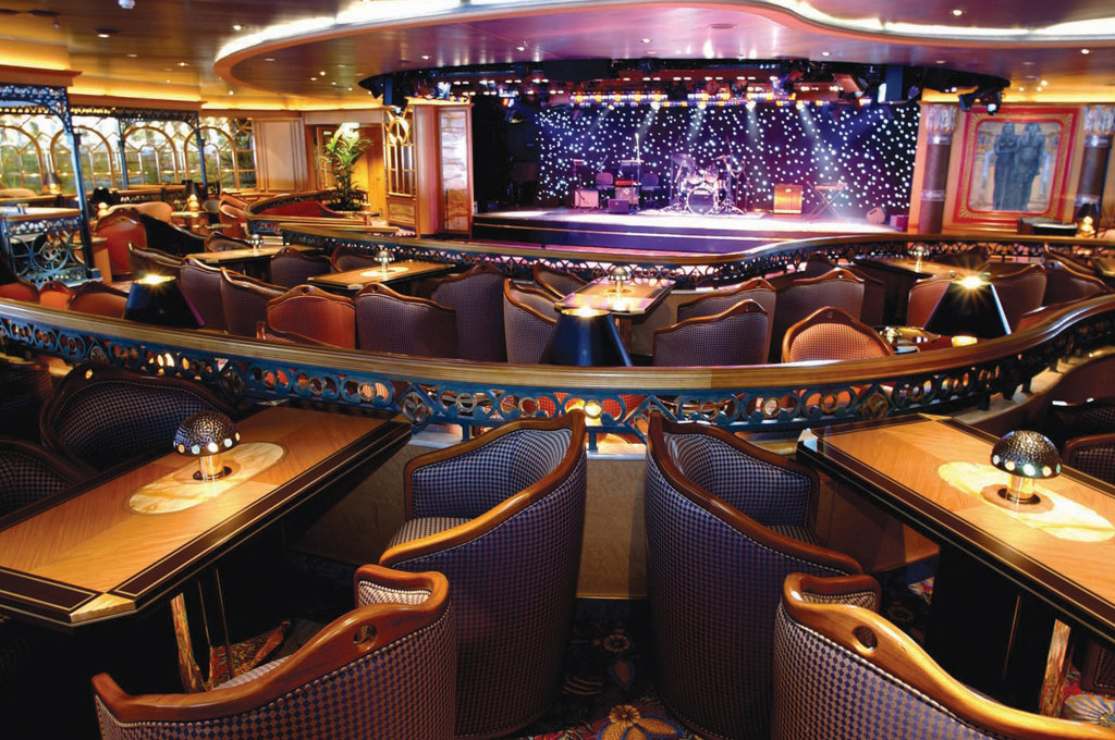 Explorers Lounge mit Showbühne, mehreren Ebenen und Polsterstühlen für Live-Darbietungen.