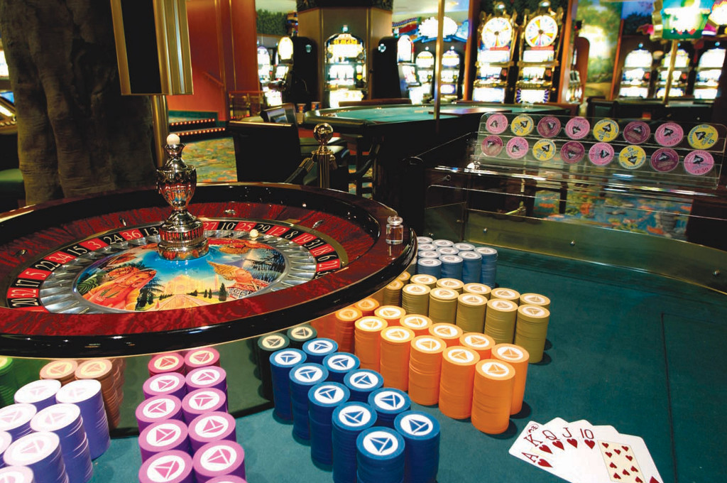 Bordcasino mit Roulettetisch, aufgestapelten Jetons, Spielkarten und Spielautomaten im Hintergrund.