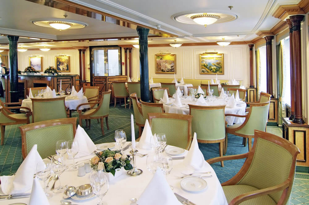 Festlich gedecktes Hauptrestaurant der Sea Cloud II mit runden Tischen, weißen Tischdecken und grünen Polsterstühlen.