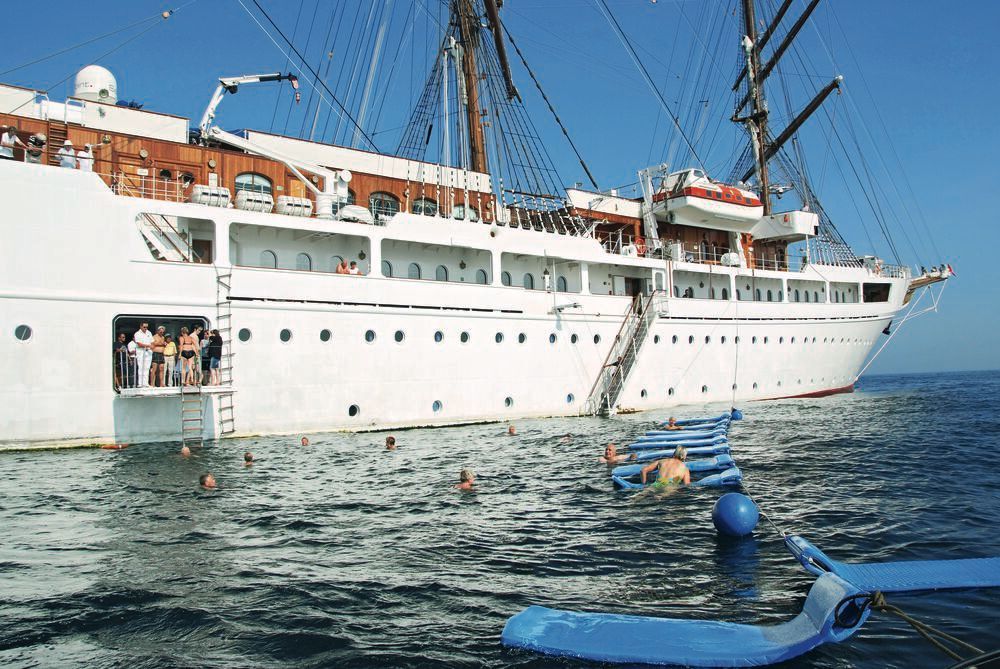 Badestopp an der Badeplattform eines vor Anker liegenden Großseglers, Gäste schwimmen neben der schwimmenden Badeinsel.