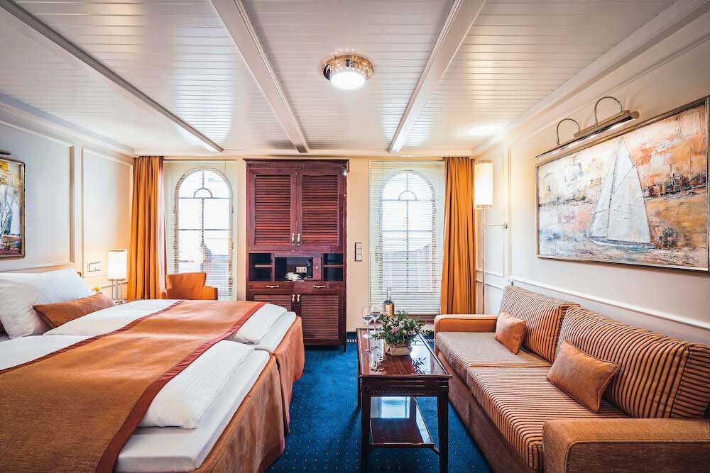 Geräumige Junior-Suite mit Doppelbett, großen Bogenfenstern und klassischer Holzmöblierung.