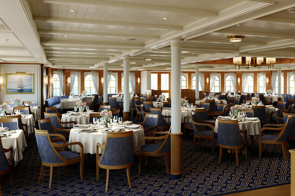 Helles Restaurant eines Segelkreuzfahrtschiffes mit blauen Armlehnenstühlen, weißen Tischdecken und Rundbogenfenstern