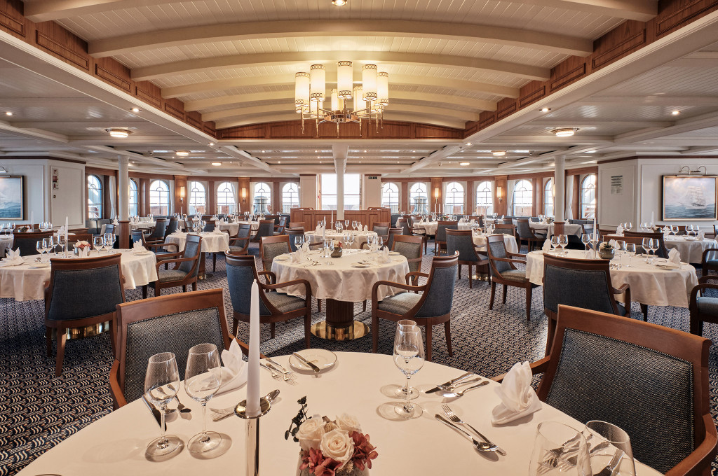 Elegantes Hauptrestaurant der Sea Cloud Spirit mit festlich gedeckten runden Tischen und Bogenfenstern.