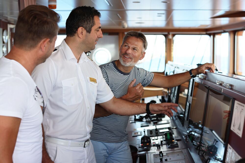 Ein Schiffsoffizier erklärt zwei Gästen auf der Kommandobrücke die Navigationsinstrumente.