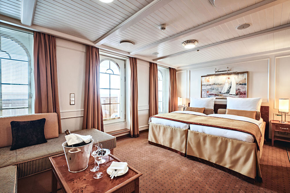 Elegante Suite mit Doppelbett, großen Bogenfenstern, Sofa und Champagnerkübel auf einem Kreuzfahrtschiff.