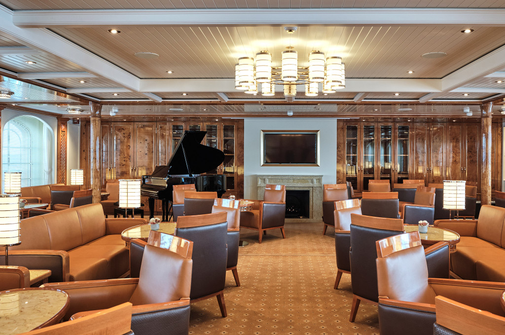 Elegante Lounge der Sea Cloud Spirit mit schwarzem Flügel, Ledersesseln, Kamin und warmem Kronleuchter.