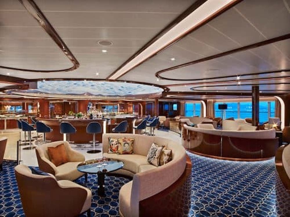 Elegante Bar mit Rundtheke, geschwungenen Sofas und Panoramafenstern mit Meerblick auf einem Luxuskreuzfahrtschiff