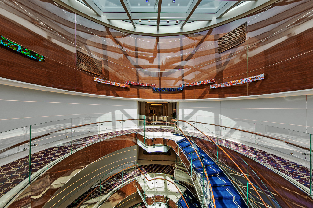 Weitläufiges Atrium der Seabourn Ovation mit geschwungener Treppe, Holzverkleidung und Glasgeländer über mehrere Decks.