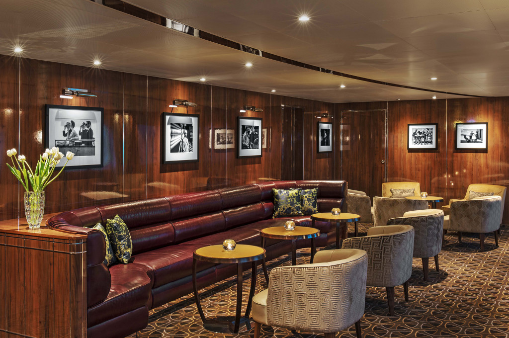 Lounge-Bereich des The Grill by Thomas Keller auf der Seabourn Ovation mit Ledersofa, Sesseln und Schwarzweiß-Fotografien.