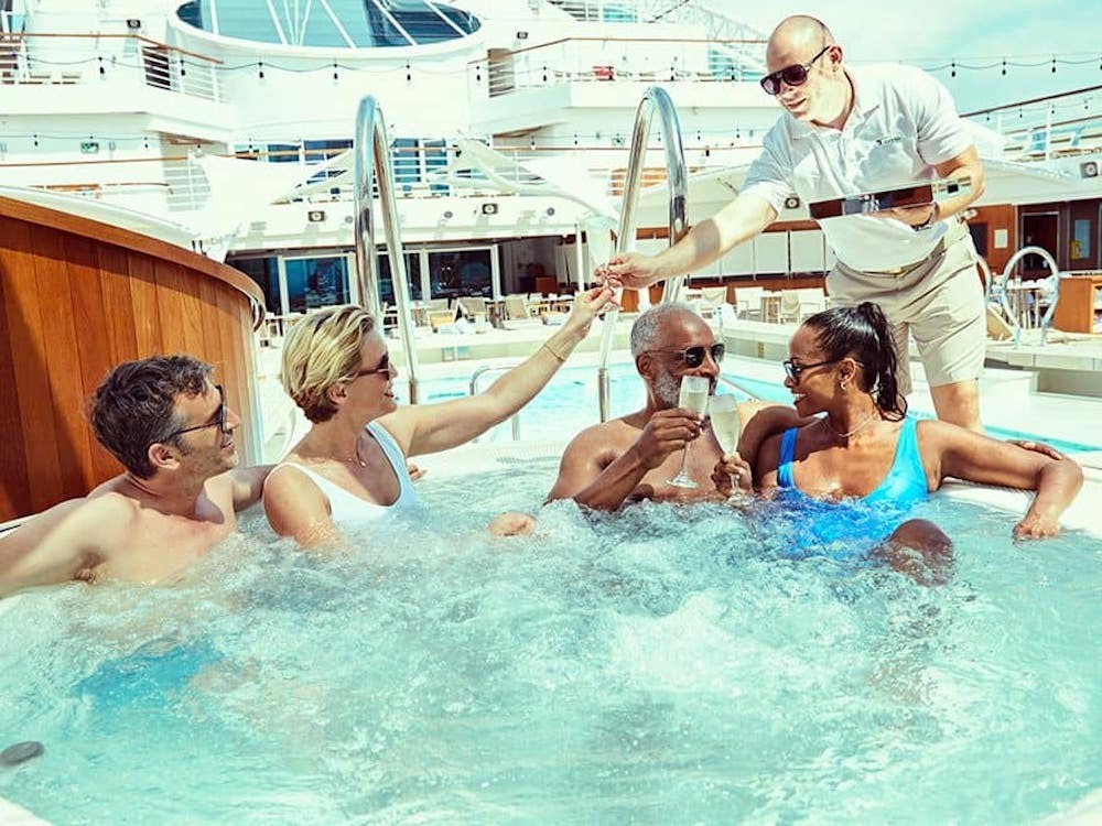 Gäste stoßen im Außen-Whirlpool der Seabourn Ovation mit Champagner an, serviert von einem Besatzungsmitglied
