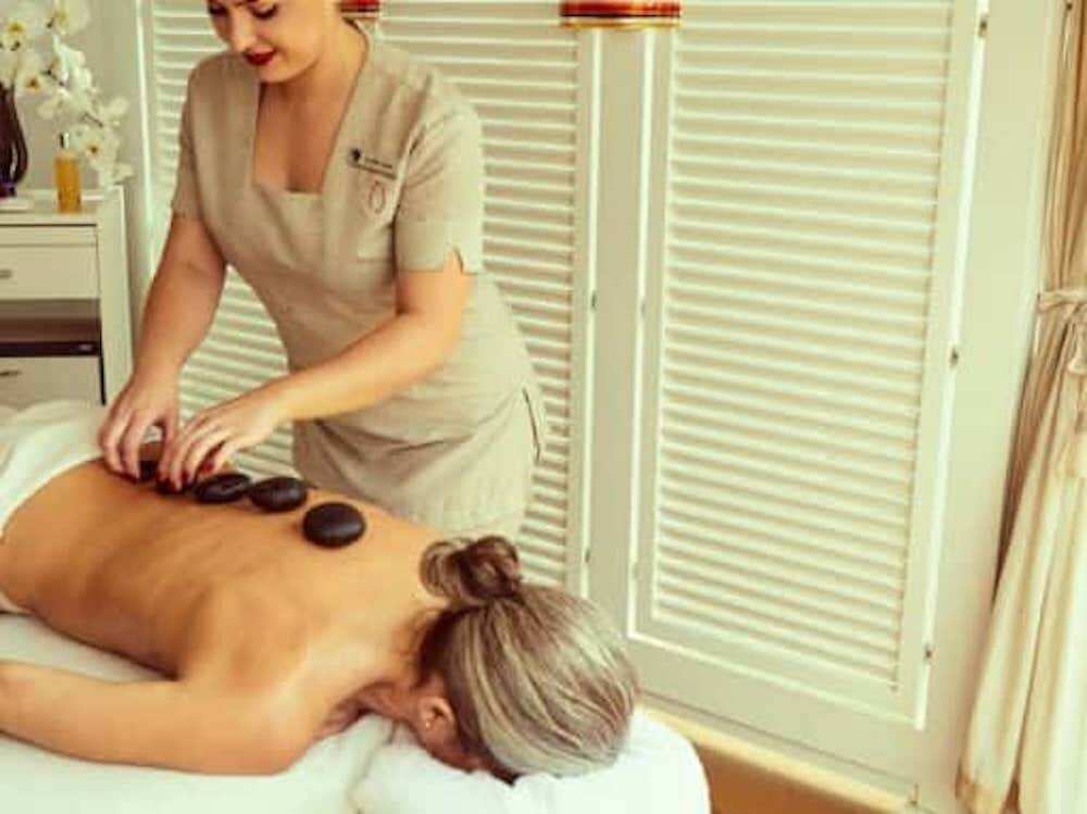 Therapeutin legt heiße Steine auf den Rücken einer Gästin im Spa-Behandlungsraum an Bord.