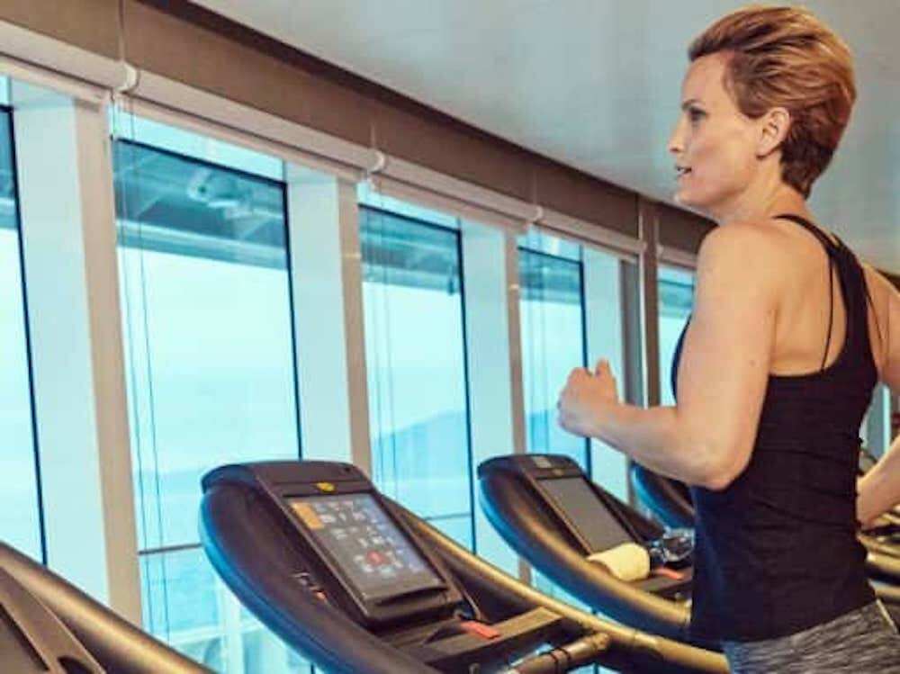 Frau trainiert auf einem Laufband im Fitnesscenter mit Panoramablick auf das Meer.
