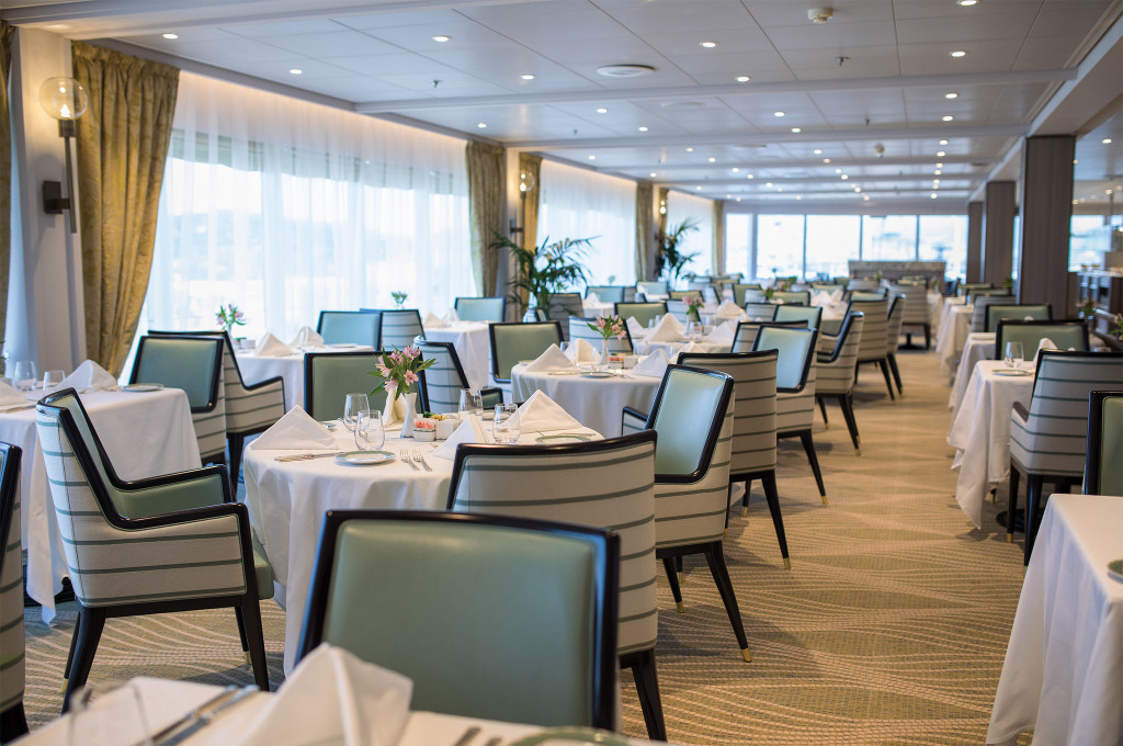 Restaurant La Veranda mit weiß eingedeckten Tischen, hellgrünen Polsterstühlen und großen Panoramafenstern an Bord der Seven Seas Mariner.