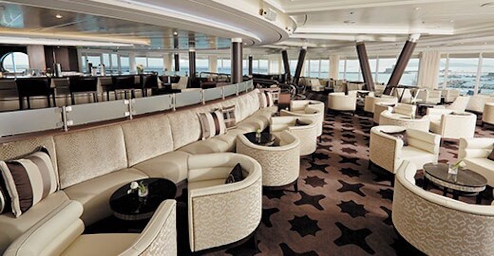 Großzügige Panoramalounge mit cremefarbenen Sofas, Rundsesseln und Blick auf das offene Meer auf einem Luxuskreuzfahrtschiff