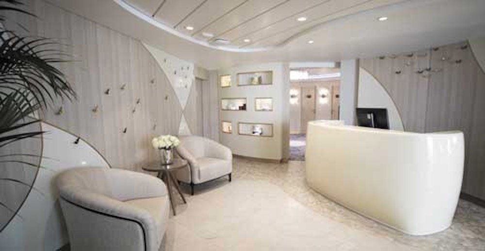 Heller Spa-Empfangsbereich mit geschwungenem weißem Tresen, Creme-Sesseln und minimalistischer Wandgestaltung auf der Seven Seas Mariner
