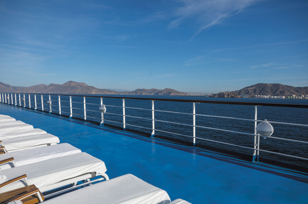 Reihe weißer Liegestühle auf dem Aussichtsdeck der Seven Seas Mariner mit Blick auf eine bergige Küstenlandschaft.