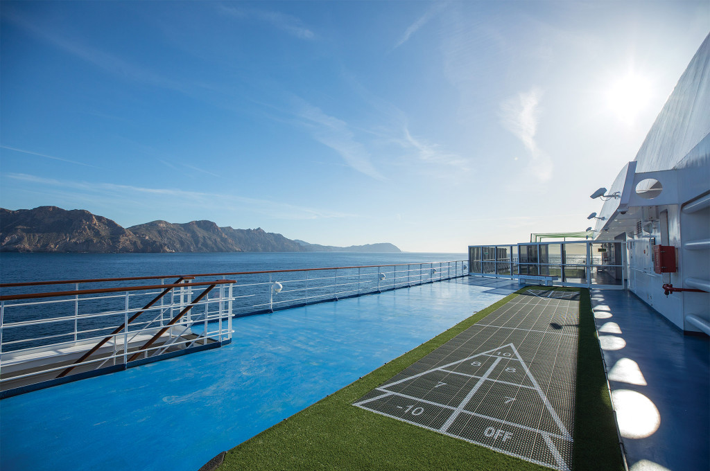 Shuffleboard-Spielfeld auf dem Außendeck der Seven Seas Mariner mit Blick auf eine bergige Küstenlandschaft.