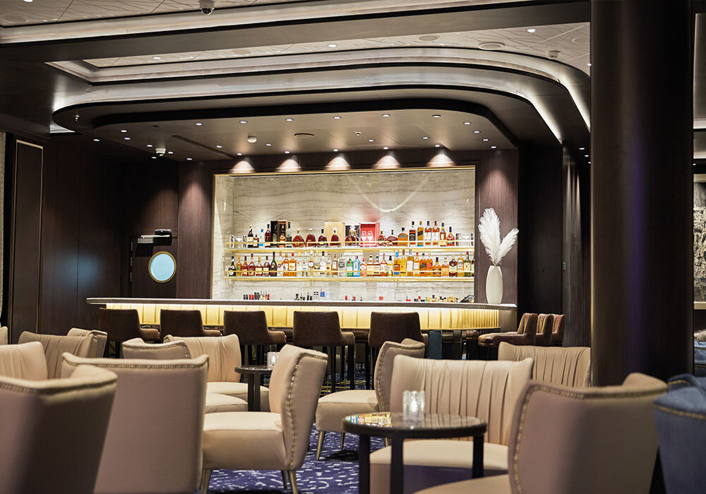 Elegante Bar-Lounge der Seven Seas Splendor mit beleuchtetem Spirituosenregal, Marmorrückwand und cremefarbenen Sesseln