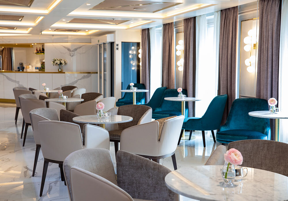 Elegantes Café-Lounge mit Marmortischen, türkisfarbenen Samtsesseln und Pendelleuchten
