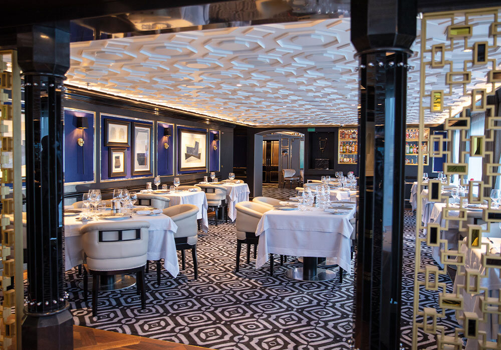 Exklusives Spezialitätenrestaurant der Seven Seas Splendor mit weißen Tischdecken, dunklen Wänden und Goldakzenten