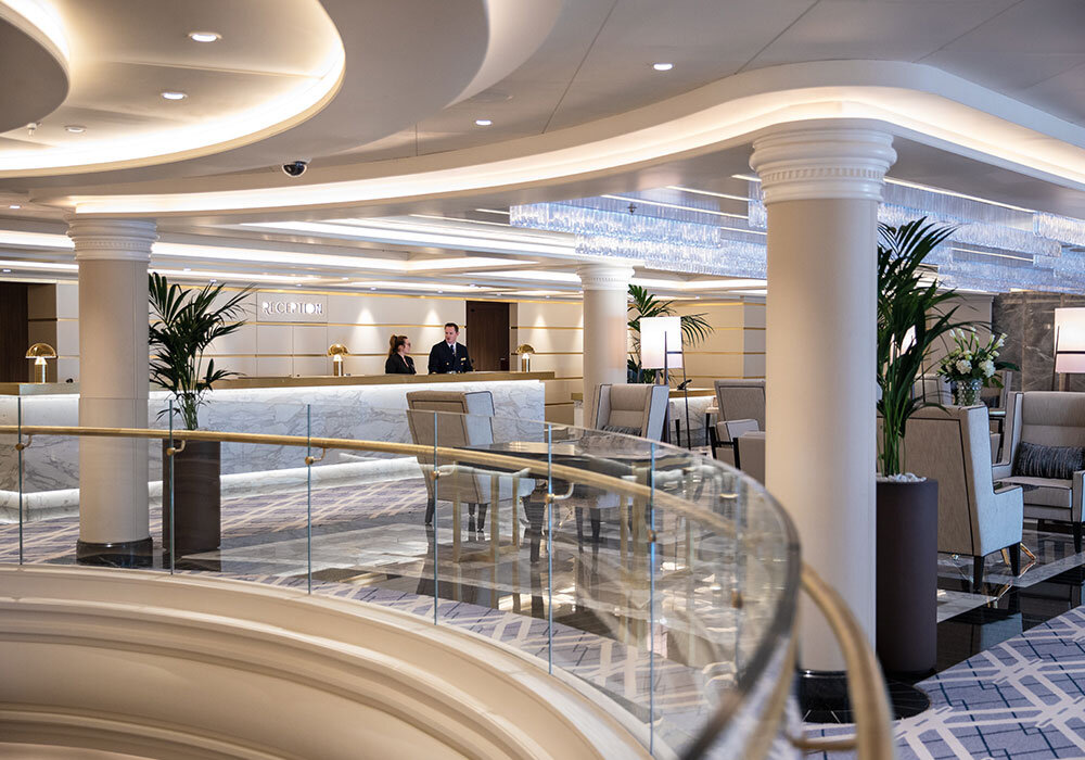 Prachtvolles Atrium der Seven Seas Splendor mit Marmor-Rezeptionstresen, geschwungener Treppe und Kristallleuchter