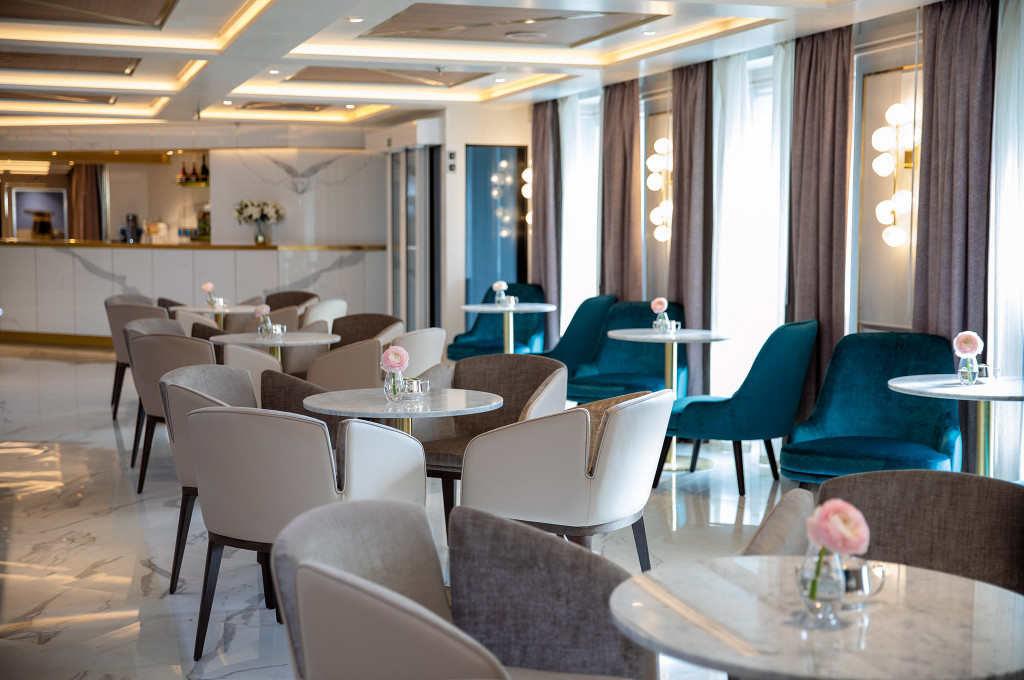 Coffee Connection mit hellen Sesseln, kleinen Marmortischen und Theke in eleganter Atmosphäre.