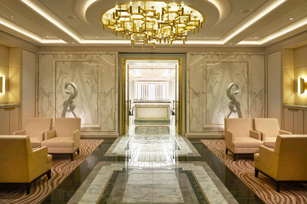 Eleganter Atrium-Eingangsbereich mit Marmorwänden, Skulpturen und großem Deckenleuchter.