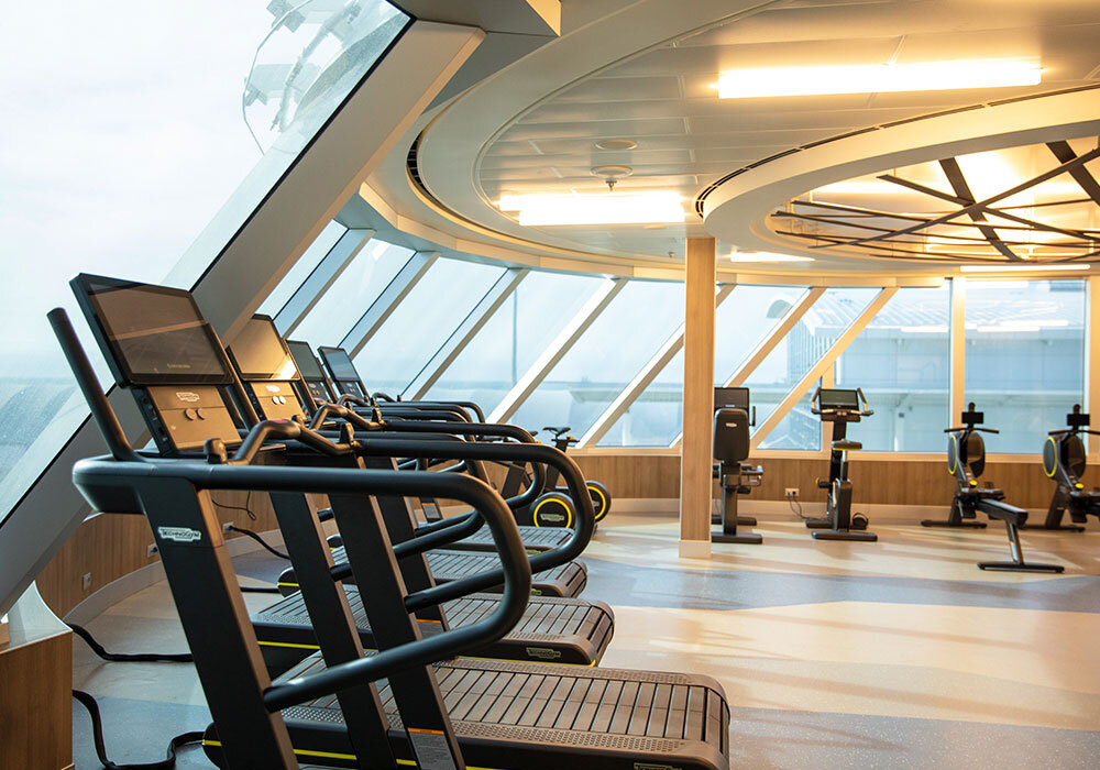 Fitnessraum der Seven Seas Splendor mit Laufbändern, Cardiogeräten und schrägen Panoramafenstern