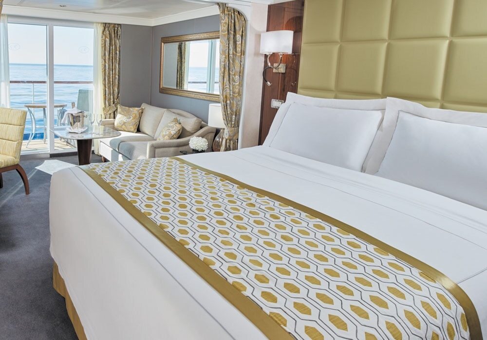 Elegante Concierge Suite mit Doppelbett, gepunkteter Tagesdecke, Sitzecke und Balkon mit Meeresblick