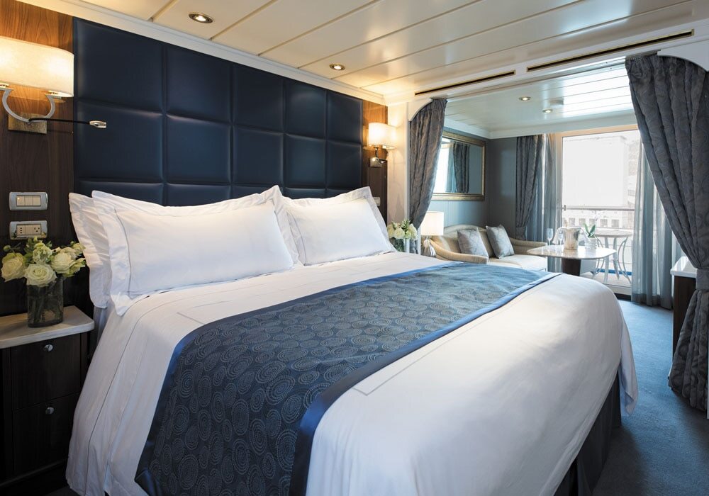 Luxuriöse Deluxe Veranda Suite mit Doppelbett, dunkelblauem Polsterkopfteil, Sofa und Balkonzugang