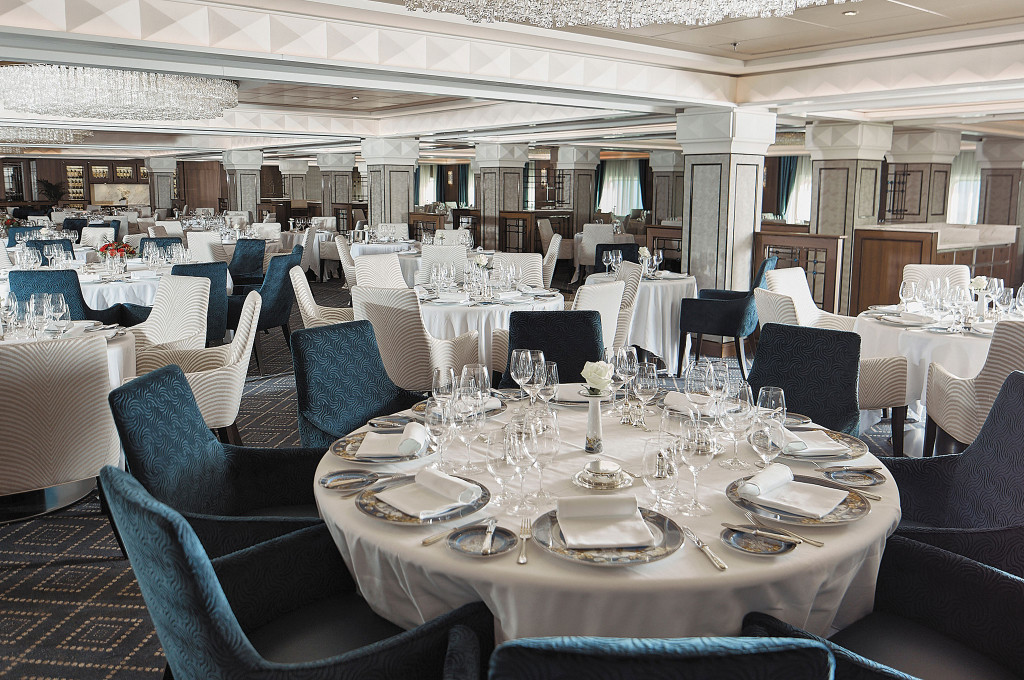 Restaurant Compass Rose mit eingedeckten Tischen, Stoffsesseln und Kristallleuchtern an der Decke.